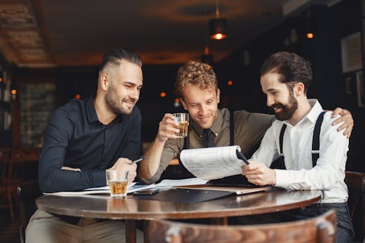 Men Sitting on a Round Table Holding Paper Printout While Having Drinks